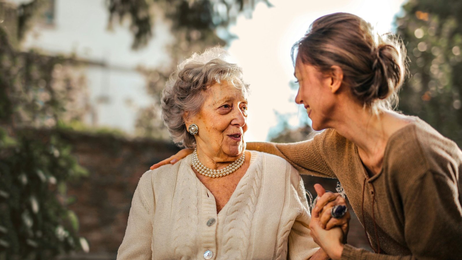 Elderly woman and adult daughter share a joyful, affectionate moment in a sunny garden.